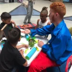 A man with red hair sitting at a table with children.