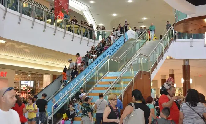 A crowd of people standing on an escalator in a mall.