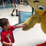 A young boy shakes hands with a mascot at a mall.