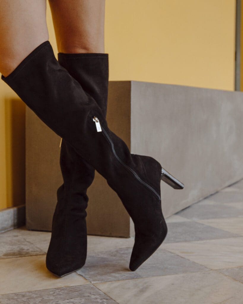 Black suede thigh high boots on a yellow background.