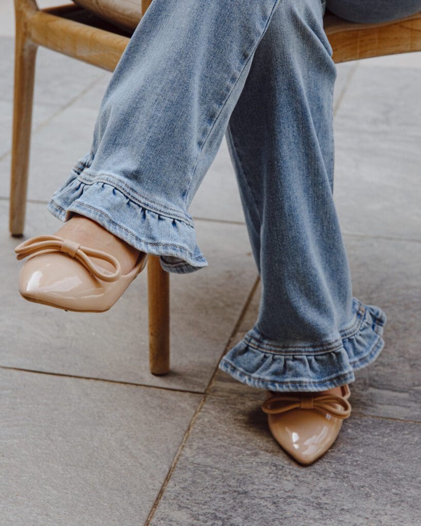 A woman sitting on a chair wearing jeans and ruffled shoes.